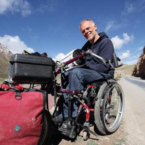 Der Reisejournalist Andreas Pröve sitzt in seinem Rollstuhl auf einer staubigen Landstraße im Hochland von Tibet - Foto: Andreas Pröve