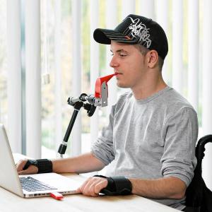 LIFEtool (Ein junger Mann sitzt am Tisch vor seinem Laptop und bedient das Gerät mit einer Mundsteuerung)