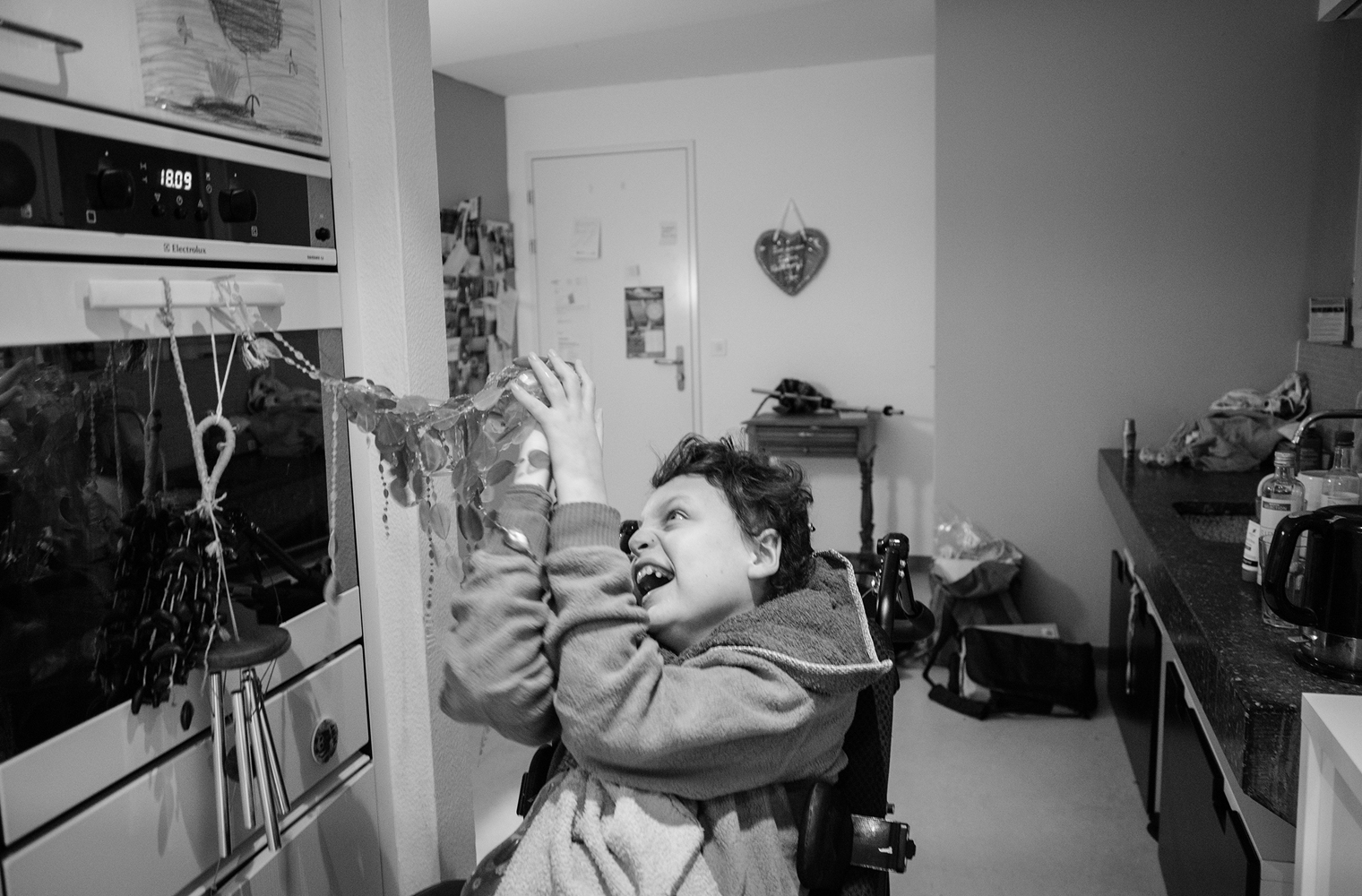 Der im Rollstuhl sitzende Yorick zieht mit freudigem Gesicht an Raschelketten, die in seiner Augenhöhe am Griff eines Küchenherdes festgemacht sind.