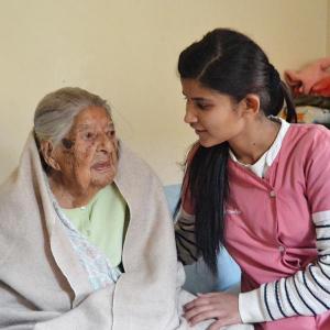 Haus für Menschen mit Demenz in Nepal - Lea Frei: Eine junge nepalesische Pflegerin sitzt neben einer älteren Frau, die in eine Decke eingehüllt is...