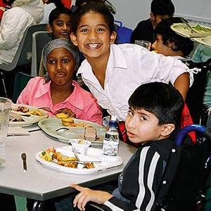 Kinder mit unterschiedlichen Hautfarben sitzen am Mittagstisch und lachen fröhlich in die Kamera. Foto: Linda Jordan