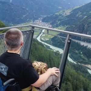 Manfred W.K. Fischer: Der Autor sitzt in seinem Rollstuhl auf einer Aussichtsrampe und genießt den weiten Blick in ein unter ihm liegendes Flusstal...